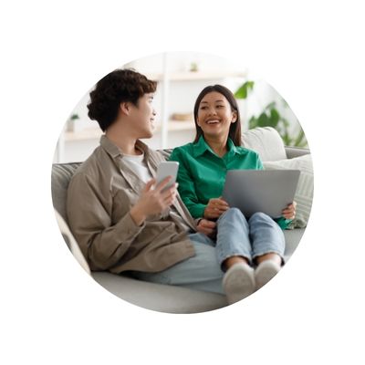 young asian adult couple sitting on sofa smiling and holding mobile devices